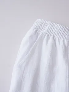 Detailed view of white cotton linen trousers featuring elastic waist and pocket