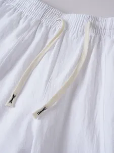 Close-up of white cotton linen trousers showing elastic waistband and drawstring detail.