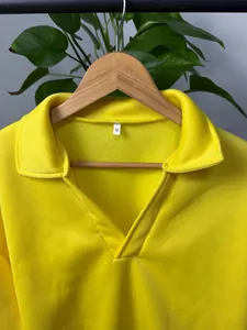 Detalle de sudadera amarilla con cuello clásico y escote en V en una percha madera