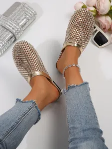 Close-up detail of glittering gold rhinestone flat mules styled with jeans and anklet