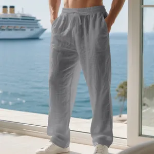 Men's loose grey linen casual pants displayed in a sunny seaside vacation setting