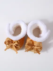 Detailansicht von warmen orangefarbenen Babystiefeln mit weißem Kunstfell und goldener Schleife