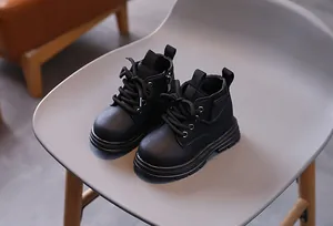 Close-up of premium black toddler Martin boots with lace-up detail and side zipper on a chair