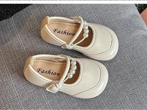 Detailaufnahme von cremefarbenen Mädchen-Mary-Janes mit eleganten Perlenriemen.