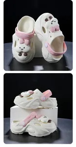 Nahaufnahme der weißen Kinderclogs mit niedlichen Wolkenanhängern und rosa Schleifen.