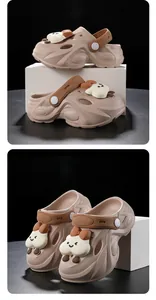 Nahaufnahme von khakifarbenen Kinder-Clogs mit niedlichen weißen Wolken-Cartoon-Anhängern.
