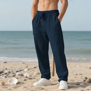Men's loose navy blue linen beach pants with drawstring waist shown on a sunny sandy beach