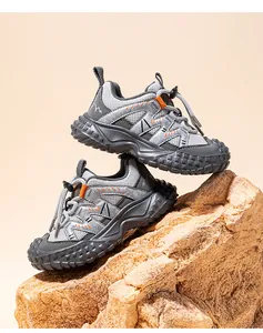 Grey and orange children's closed-toe mesh sports sneakers displayed on a decorative rock