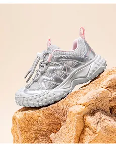 Detailed view of a silver and pink children's athletic sneaker on a textured rock