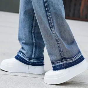 Detailed close-up of blue wide-leg denim jeans with raw hem and white sneakers