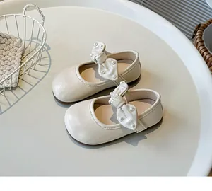 Elegante cremefarbene Mary Janes für Kleinkinder mit Perlen-Schleife auf weißer Fläche.