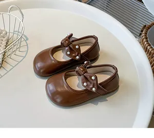 Nahaufnahme brauner Mädchen-Leder-Mary-Janes mit dekorativer Schleife und Perlen.