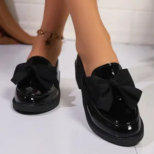 Gros plan de mocassins à plateforme en cuir verni noir avec un grand nœud élégant
