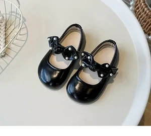 Nahaufnahme eleganter schwarzer Mädchen-Mary-Janes mit Schleife und zarten Perlenakzenten