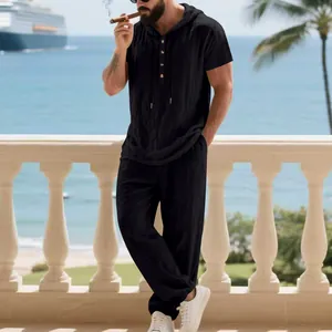 Men's black linen hooded Henley shirt and pants set in a vacation lifestyle setting