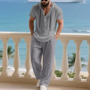 Detail view of men's grey linen hooded Henley shirt and loose pants set in a beach setting.
