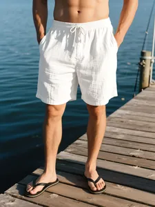 Pantalones cortos de lino blanco para hombre en un muelle de madera frente al mar azul