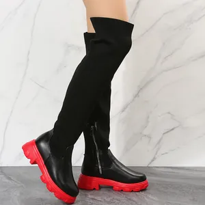 Side detail of over-the-knee boots with black knit leather patchwork and red chunky soles.