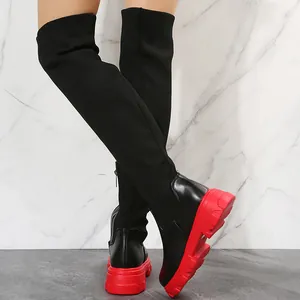 Detail view of over-the-knee boots featuring black knit upper and thick red platform sole.