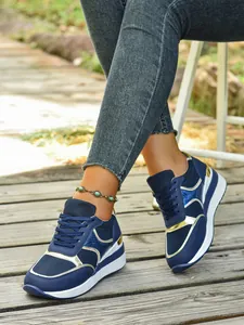Κοντινή όψη κομψών μπλε και χρυσών sneakers με σφήνα και πλέγμα σε ξύλινο δάπεδο