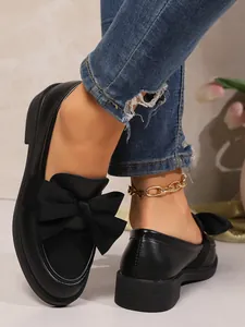 Close-up of black block heel loafers with large bow detail and thick sole