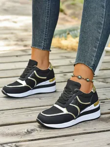 Κοντινό πλάνο μαύρων sneakers με πλατφόρμα και χρυσές λεπτομέρειες σε ξύλινο δάπεδο.