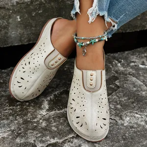 Close-up of beige laser-cut mules with metal studs and intricate hollow patterns.