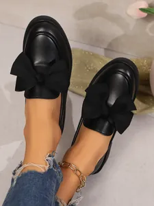 Close-up shot of women's black retro loafers featuring oversized bows and thick soles.