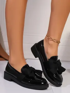 Detailed view of women's black retro loafers featuring a large bow and thick block heel