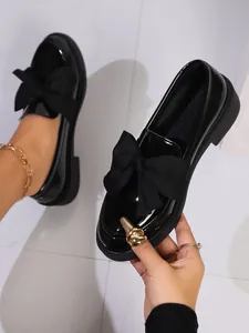 Close-up of black patent leather loafers with a stylish oversized bow decoration