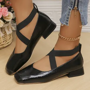 Close-up view of black patent leather Mary Jane flats featuring criss-cross elastic straps.