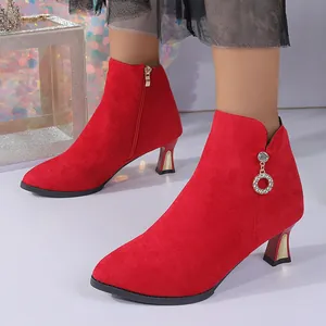 Nahaufnahme von roten Wildleder-Stiefeletten mit Pfennigabsatz und Strass-Anhänger.