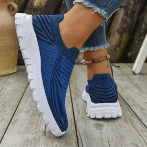Close-up of blue breathable knitted slip-on sneakers with white soles on wooden deck.