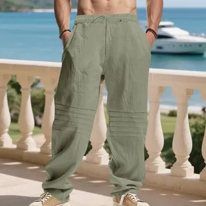 Men's loose linen pants with pleated thigh details shown in a seaside vacation setting