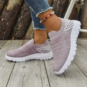 Close-up of mauve knit slip-on sneakers worn on a wooden deck background.
