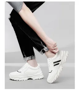 Vue de profil de baskets blanches à rayures noires et semelles compensées sur fond gris.