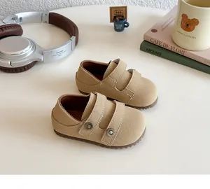 Cozy lifestyle shot of tan suede toddler loafers with double Velcro straps on a desk.