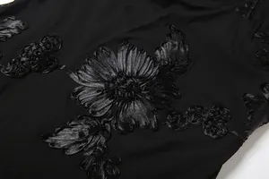 Detailed close-up of intricate black ribbon flower embroidery on mesh summer dress fabric.