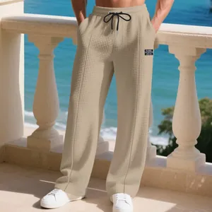 Detail view of men's waffle-textured beige wide-leg trousers on a coastal balcony.