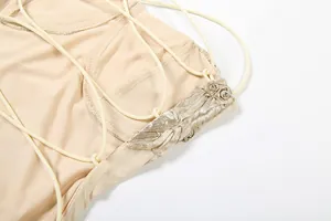 Close-up detail of a beige backless dress featuring lace-up straps and gold floral patch.