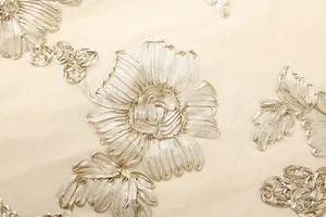 Detailed view of elegant ribbon floral embroidery on a sheer cream mesh fabric.