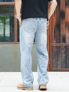 Back view of men's loose straight-leg light blue denim jeans in a casual outdoor setting