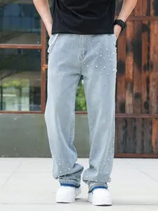 Detail view of light blue men's loose jeans with white pearl beading accents