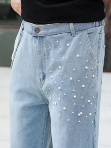 Close-up of light blue straight denim jeans featuring decorative white pearl beadings.