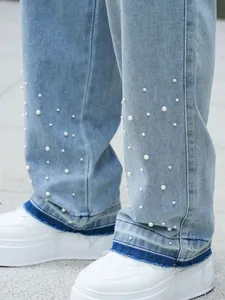 Detailed shot of light blue denim pants with white pearl embellishments and fringe raw hem
