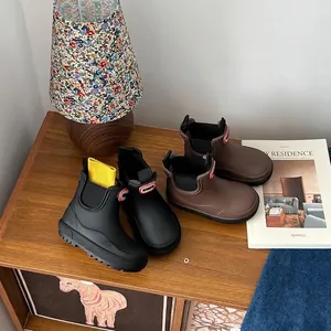 Kids' waterproof Chelsea-style rain boots in matte black and brown displayed on wooden surface