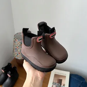 Detailed view of brown children's waterproof Martin-style rain boots held by hand