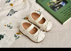 Primer plano de zapatos Mary Jane crema para niñas con lazos y banda elástica