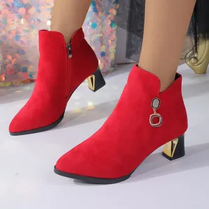 Detalle de botines rojos de ante con punta afilada y tacón de bloque con detalles oro.