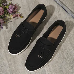 Detailed top view of black suede flat loafers with decorative tassels and white soles